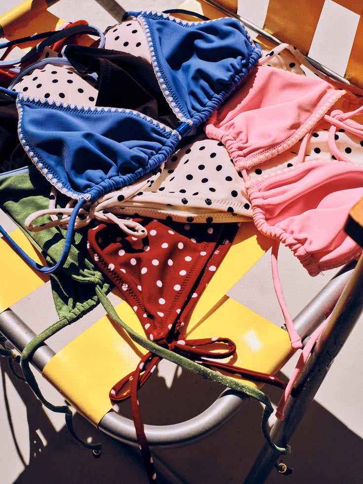 Colourful swim tops piled on a yellow and white striped chair in the sun