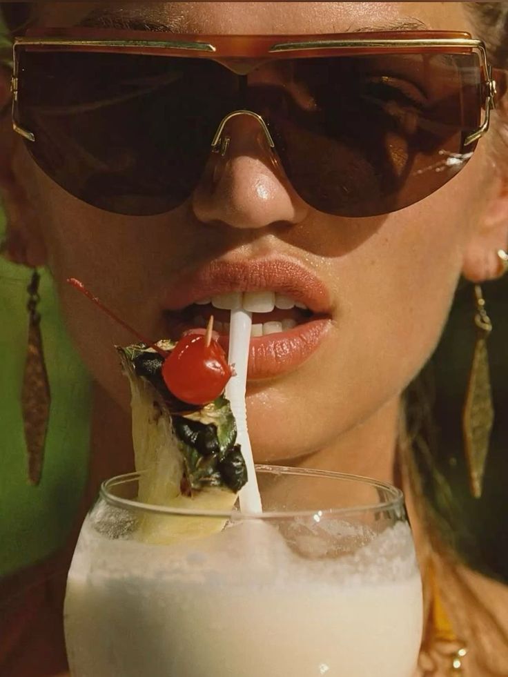 Close-up of a woman in sunglasses sipping a pina colada with a cherry and pineapple